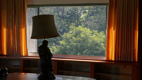 view from a cozy bedroom, complete with warm lamps, vibrant orange curtains, and a breathtaking natural forest landscape just outside the window