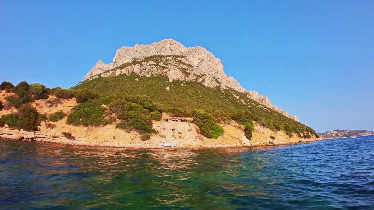 Navigando su acque calme e trasparenti verso la maestosa isola calcarea di Tavolara sotto un cielo azzurro e limpido in una giornata di sole in Sardegna, Italia