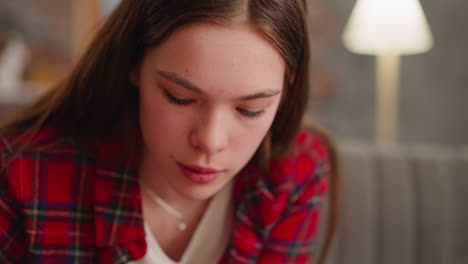 young woman in red checkered shirt looks down in living room