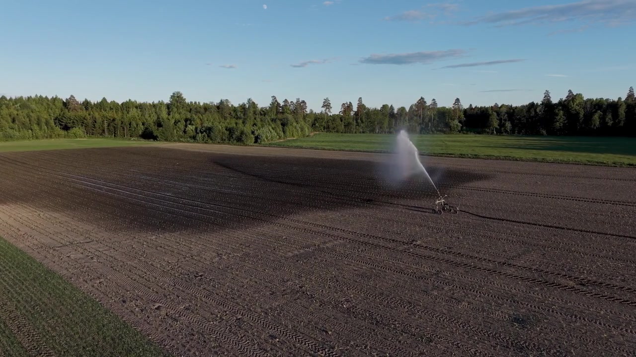 Una ripresa al rallentatore con drone di una macchina per l'irrigazione che annaffia un campo, illuminata dalla splendida luce dell'ora d'oro