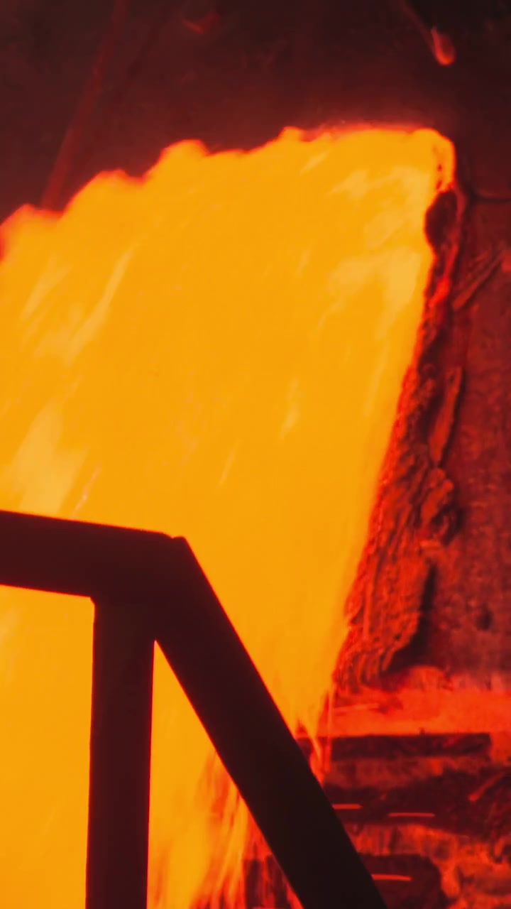 Metallo fuso che cola dietro una ringhiera di sicurezza in un'area di contenimento con bagliore arancione e atmosfera fumosa.