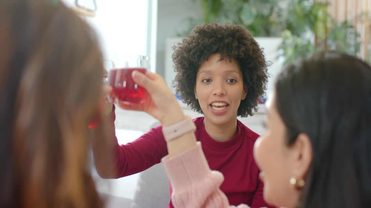 Donna in borgogna che alza un bicchiere rosso brindando sul divano, che reagisce all'amico che alza il palmo interrompendola