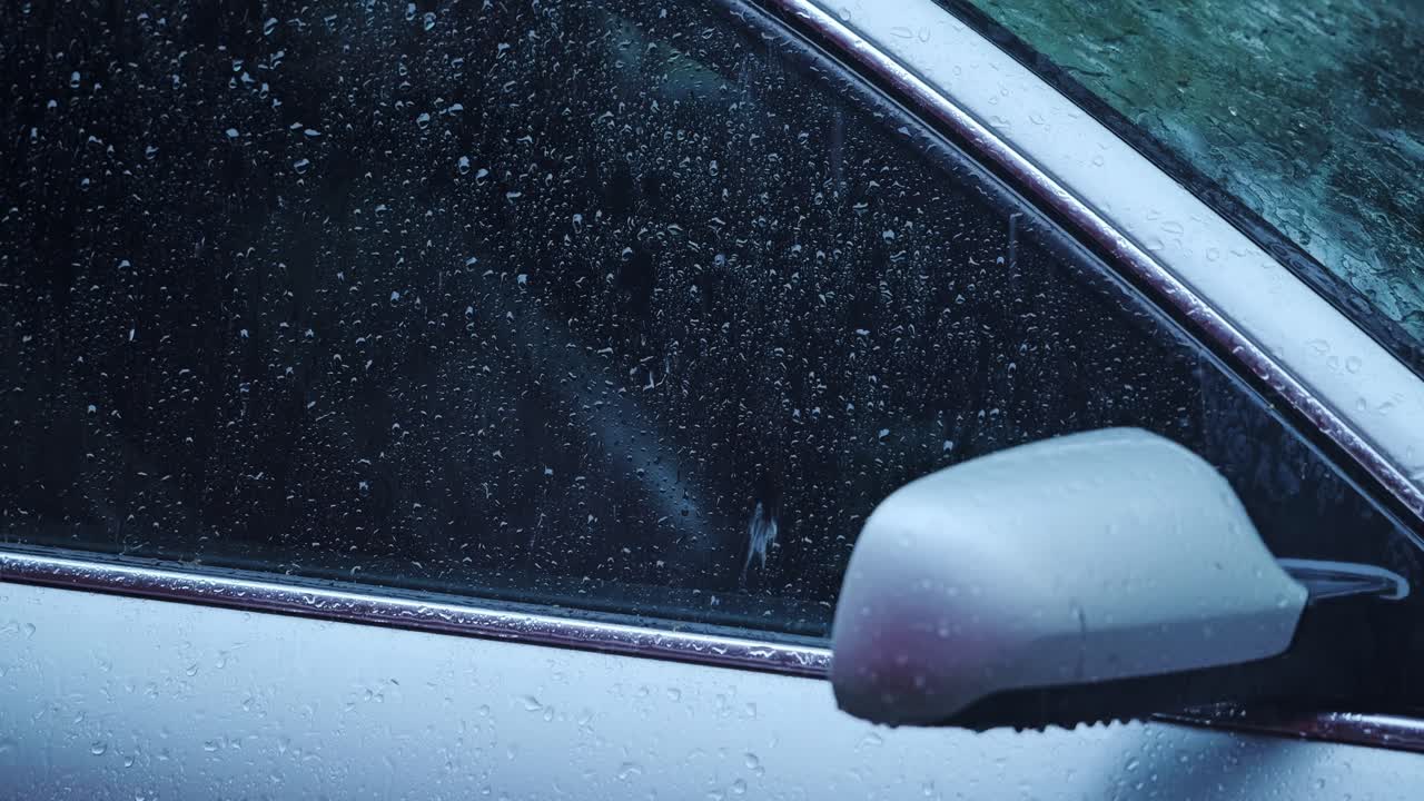 Raindrops form gentle trails on car glass during cinematic slow motion rainfall