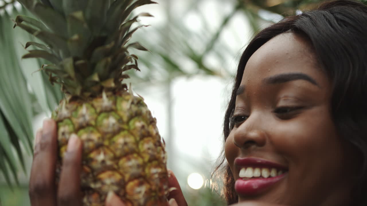 Shooting close up young beautiful girl holding a pineapple and smiling at the camera against the