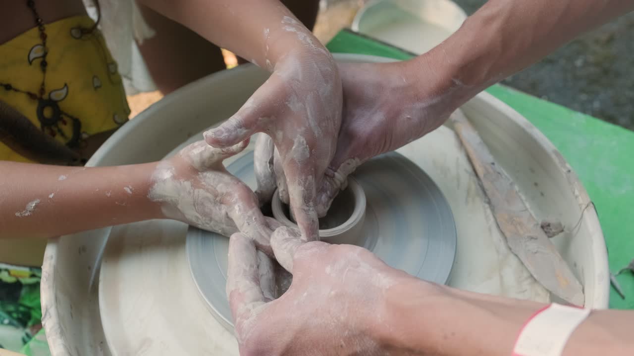 cerca de las manos trabajando con arcilla en la rueda de un alfarero. artesano con niño da forma a un producto de arcilla en una rueda de alfarero