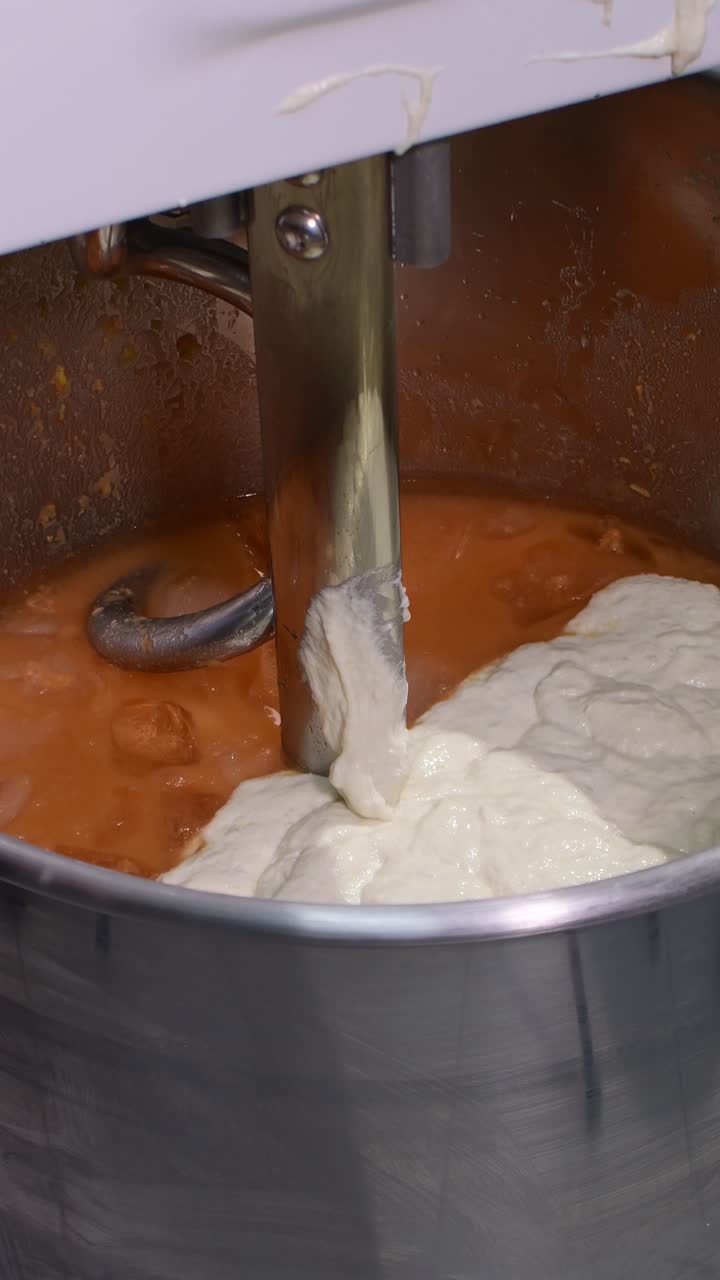 Vertical Close-up of a spatula adding sourdough starter into an industrial mixer, capturing professional bread preparation in a bakery kitchen