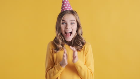 una adolescente caucásica con un sombrero de fiesta y aplaudiendo.