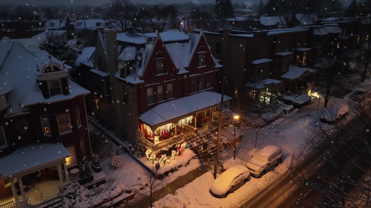 Snowy residential area with lighting house decorated during christmas season. Quiet neighborhood in USA with festive decorated porch entrance. Aerial approaching shot.
