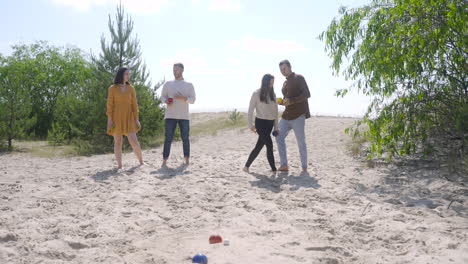 vista frontal del grupo de mujeres y hombres amigos jugando petanca en la playa en un día soleado