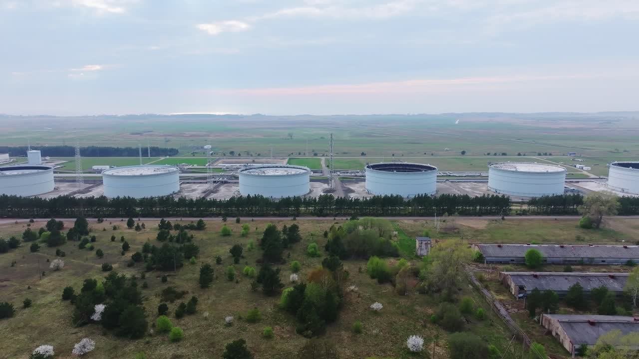 Drone flies sideways past massive oil tanks in Butinge terminal, cloudy dusk
