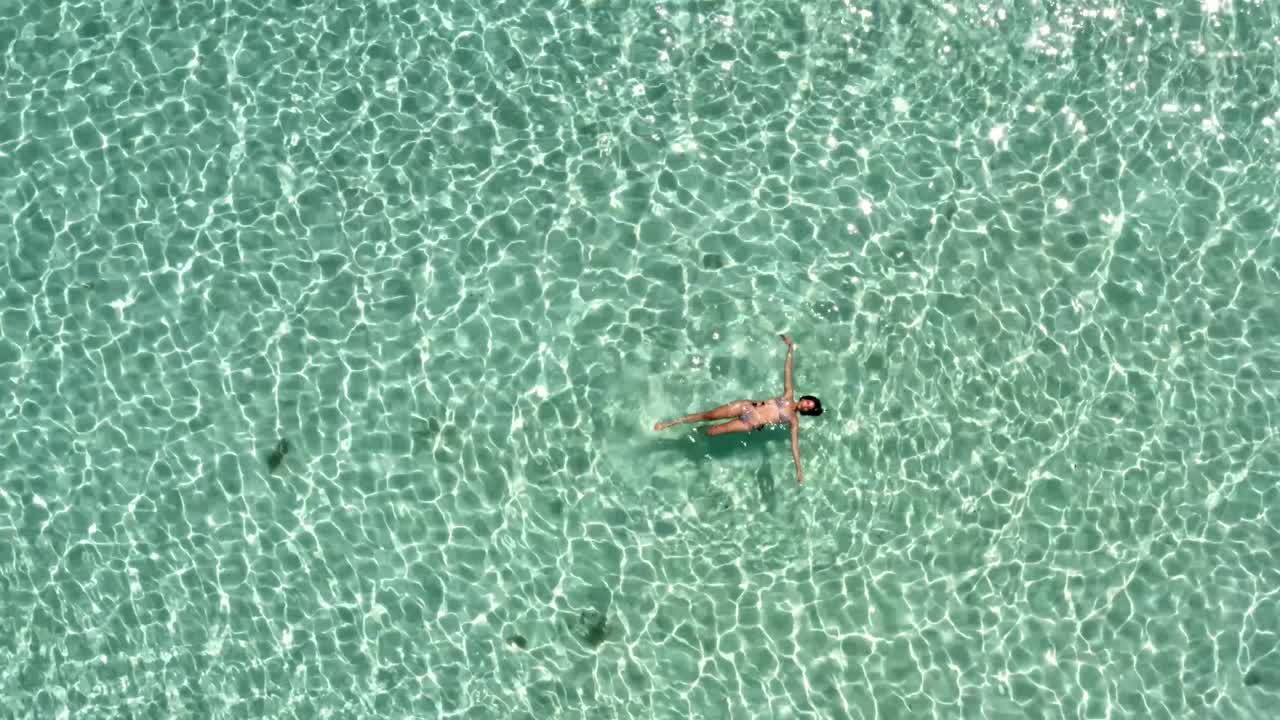 Gorgeous woman in a bikini floating on her back in the middle of a sea of crystal clear turquoise water in the beautiful nature reserve of Sian Ka'an near Tulum, Mexico