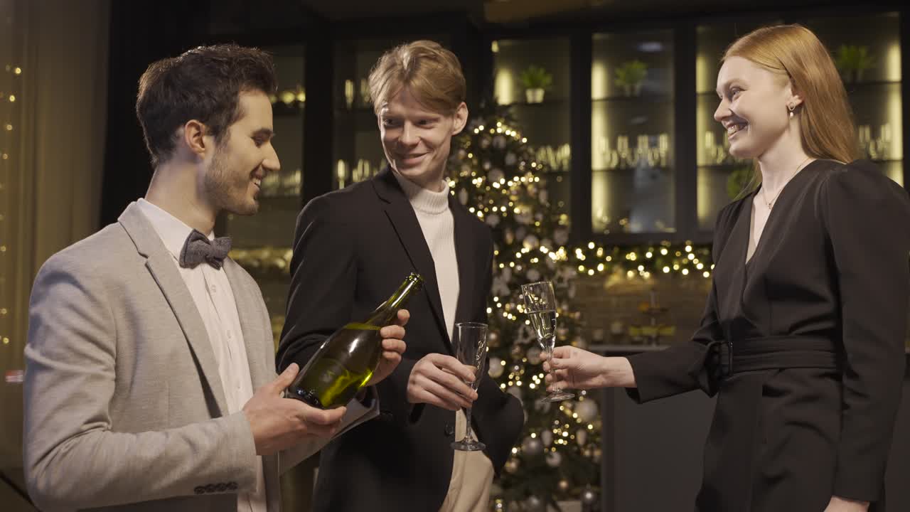 A guy pours champagne into a man's and a woman's glasses, then they toast and take a sip in new year's party