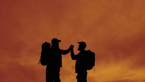 silhouetted figures with backpacks at sunset
