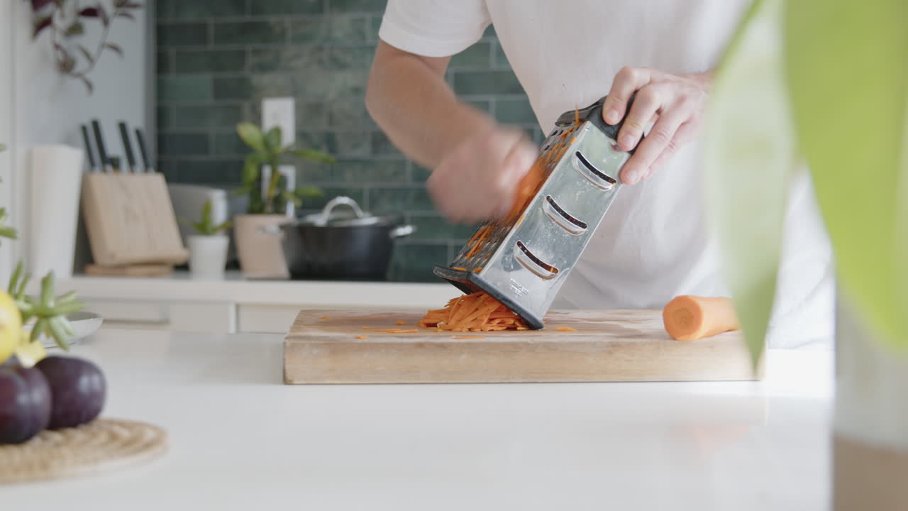 Piano medio di un uomo che grattugia carote fresche con una grattugia in una cucina moderna.