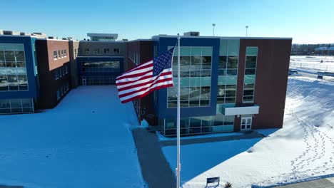 Toma-Aérea-De-Una-Bandera-Estadounidense-Junto-A-Un-Edificio-Escolar.