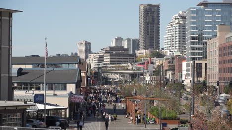 a timelapse video capturing people strolling along seattle’s waterfront and alaskan way, with the bustling cityscape in the background on a sunny day.