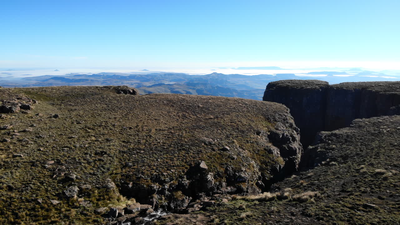 Mirador de una extensa altiplanicie al amanecer, revelando un afloramiento plano que conduce a un desfiladero profundo, con vegetación alpina escasa