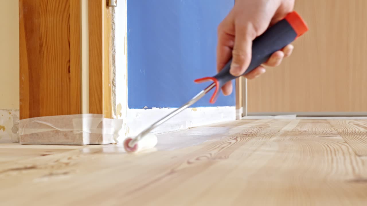 Worker Applying Varnish Coating To A Hardwood Floor Using A Roller. - closeup shot