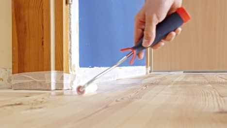 worker applying varnish coating to a hardwood floor using a roller. - closeup shot
