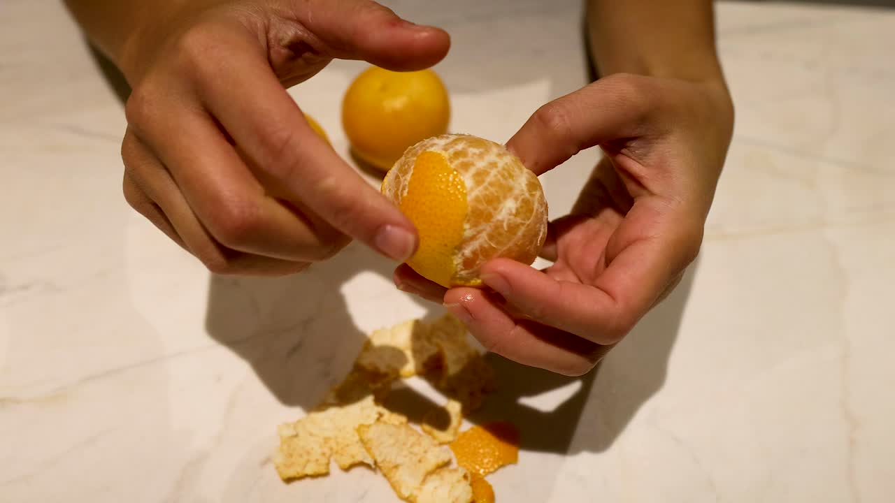 manos pelando una naranja en una encimera de mármol