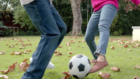 Midsection of african american mother and son playing football in garden, in slow motion