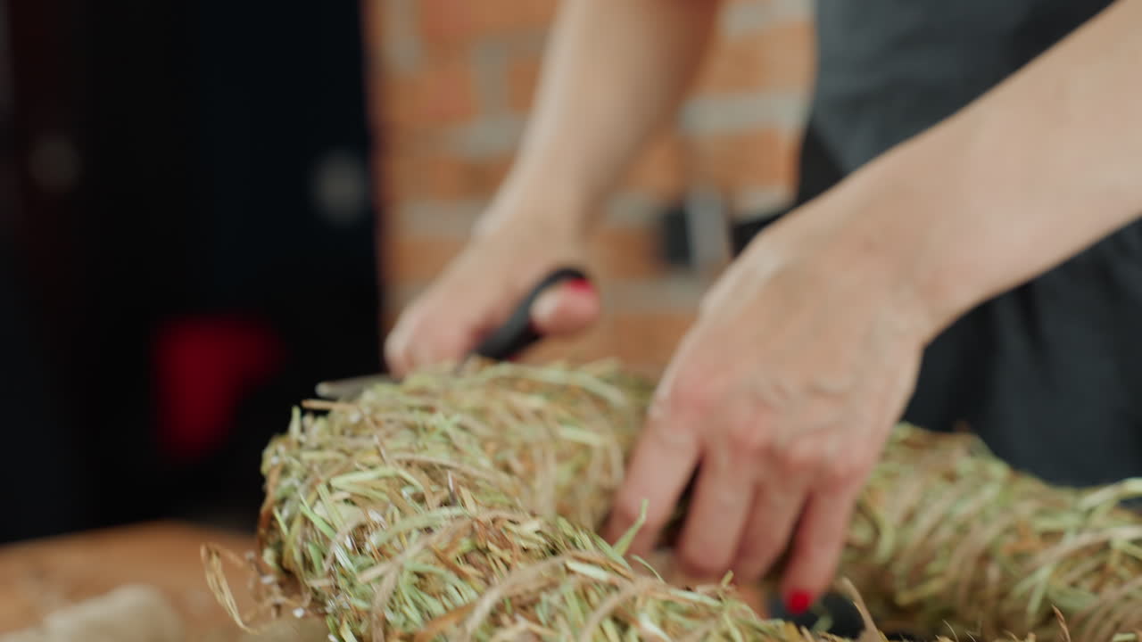 Closeup of woman holding straw wreath during crafting process, handmade decoration preparation with natural dried grass material, shaping rustic circular base for floral decorative arrangement indoors