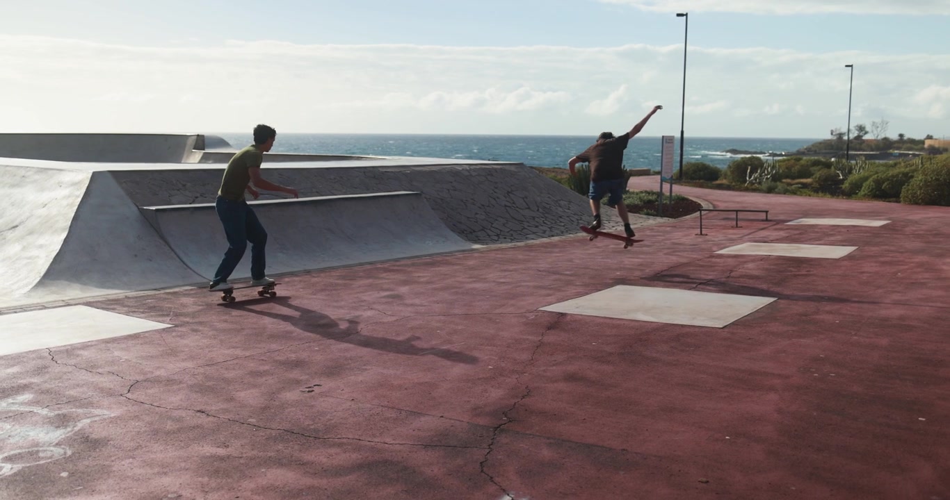 To unge mænd skater og øver tricks i en kystnær skatepark