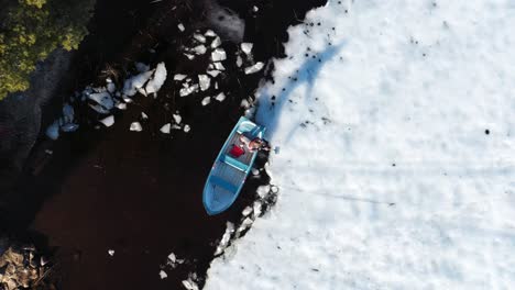 man in a boat breaking ice with shovel on a winter day