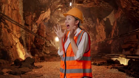 side view of asian female engineer with safety helmet smiling to camera and saying wow in underground mine tunnel