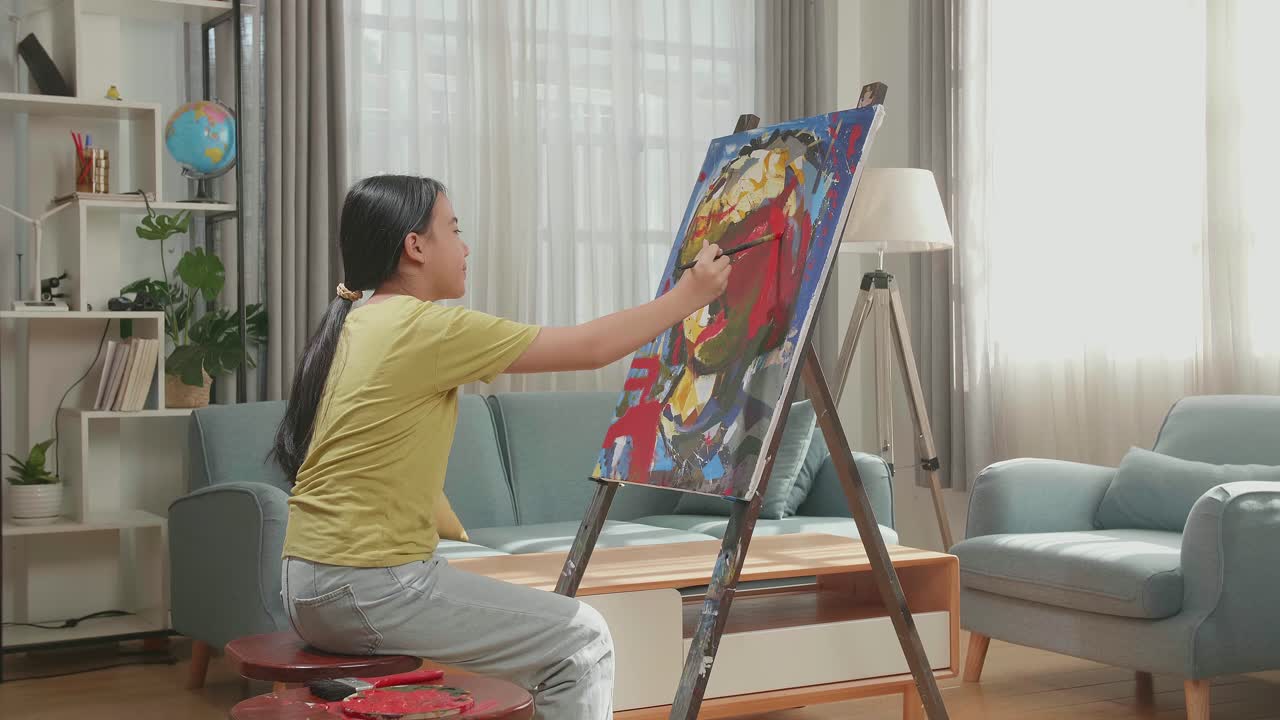 Side View Of An Asian Artist Girl Holding Paintbrush Mixed Colour And Painting A Girl'S Ear On The Canvas