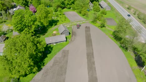 Aerial-view-of-plowed-field-with-tractor-sowing-seeds-of-wheat,-agricultural-theme,-farm-tractor-and-seeder-planting-crops-on-a-field-on-sunny-spring-day,-birdseye-drone-shot-moving-forward,-tilt-down