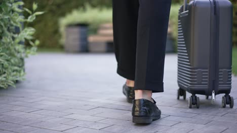 back view legs of young man walking in slow motion with travel bag. live camera follows unrecognizable caucasian businessman strolling with luggage in city park.