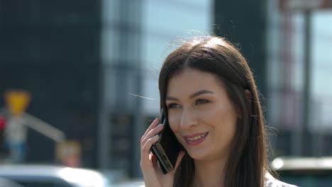 A-close-up-of-a-brunette-female,-talking-on-the-phone,-with-the-city-in-the-background