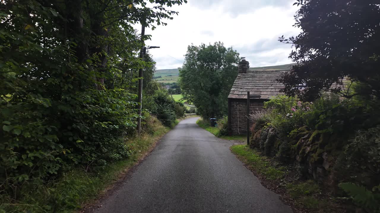 Narrow asphalt road descending between green grass and trees into a valley in County Durham, England