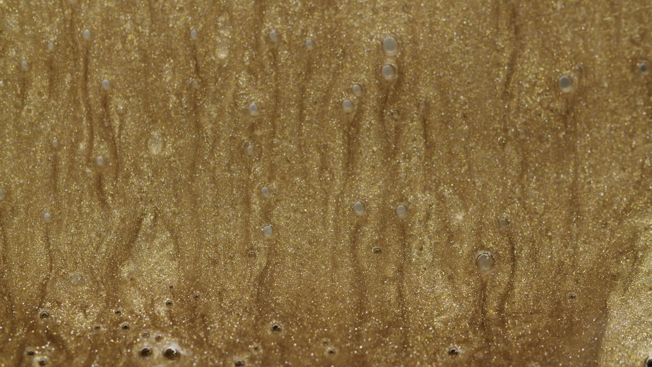 파도를 형성하고 프레임 밖으로 아래쪽으로 이동하는 황금 입자 커튼의 매크로 샷
