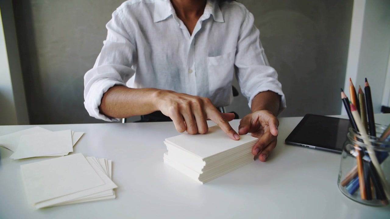 Placing stack, Asian woman in white shirt aligning cream cards at home desk, preparing materials