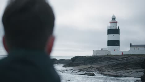 hombre caucásico de pie en la orilla y mirando un faro