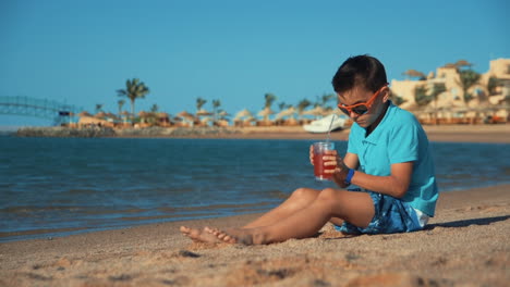 Attraktiver-Teenager-Mit-Sonnenbrille,-Der-Limonade-Am-Strand-Trinkt.-Junge-Stellt-Glas