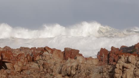 huge crashing whitewater waves break onto rocky shore on sunny day