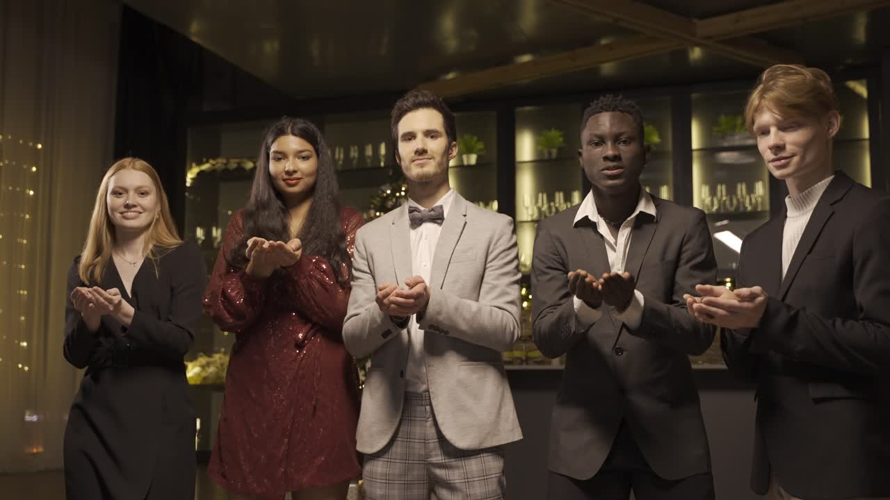 Group of friends wearing elegant clothes blow and throw conffeti while dancing and hugging each other in new year's party