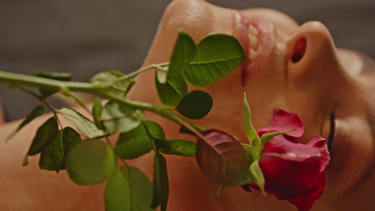 A beautiful blond woman sensually caresses her face with a red rose