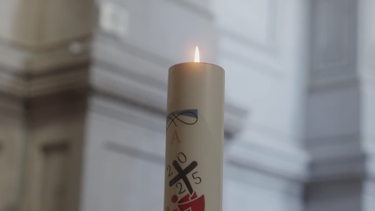 Extreme close up view of a burning decorated paschal candle featuring a cross symbol inside a bright church with blurred background