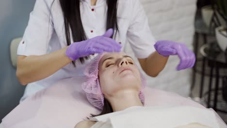 An experienced cosmetologist in sterile gloves makes a face massage to a woman on the couch in the cosmetology office. Relax. Facial Moisturizing Procedure