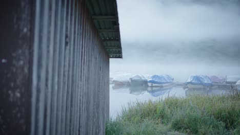 mysterious cabin by lakeside, boats moored on foggy misty lake