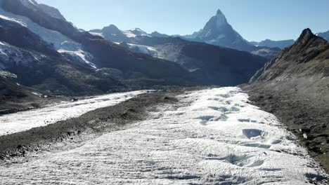 Aerial-flyover-over-the-moraines-and-crevasses-of-the-Gorner-glacier-with-a-pan-up-revealing-the-Matterhorn-in-the-background-on-a-sunny-summer-day-in-Zermatt,-Switzerland