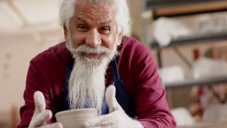 un alfarero bi-racial senior feliz trabajando en un jarrón de arcilla y sonriendo en el estudio de cerámica, en cámara lenta