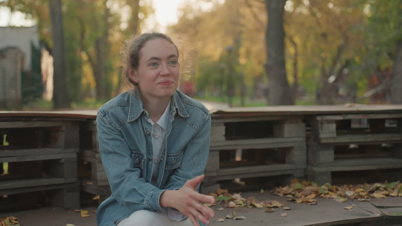 Donna si rilassa su una panchina in uno spazio verde e tranquillo. Signora calma che indossa il denim e si gode momenti felici all'aperto oggi. Donna allegra in denim seduta su una panchina si rilassa in un bellissimo ambiente lussureggiante del parco.