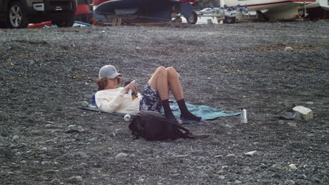 young male relaxing and using smartphone outdoor near porthallow fishing village in cornwall, england, united kingdom - wide shot