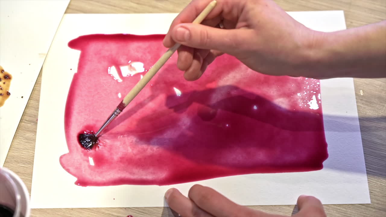 A woman in a studio painting on paper with red wine and brush, close view, slow motion