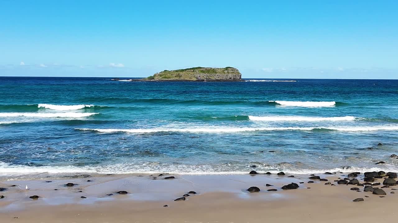 A serene ocean scene with gentle waves and a distant island under a clear blue sky.